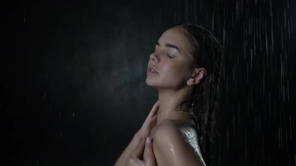 Serene attractive young woman standing under running shower water with splashes all over body. Wet millennial girl under the falling drops, standing under stream of water, beauty and body care concept — Stock Video