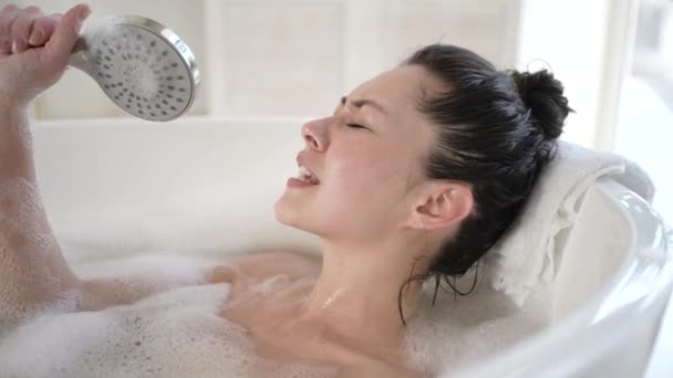 Emocionada chica asiática de raza mixta cantando en la bañera con cabezal de ducha. Feliz millennial multi étnicas mujeres que se divierten disfrutar del cuidado corporal en el baño, terapia de tratamiento de belleza y el concepto de estilo de vida saludable — Vídeo de stock