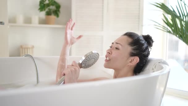 Attraente ragazza asiatica che canta nella vasca da bagno usando il soffione. Felice millenaria donna multietnica divertirsi godere di cura del corpo quotidiana in bagno, terapia di trattamento di bellezza e concetto di stile di vita sano — Video Stock