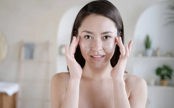 Young multi ethnic asian girl touching face with fingers apply caring about skin uses moisturiser creame. Morning routine, grooming, personal care, skincare beauty treatment bodycare cosmetics concept — Stock Photo, Image