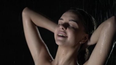 Vücudunun her tarafına su sıçrayan şehvetli ve çekici bir kız resmi. Düşen damlaların altında ıslak genç bir kadın, karanlık arka planda suyun altında duruyor, güzellik ve sağlık konsepti..