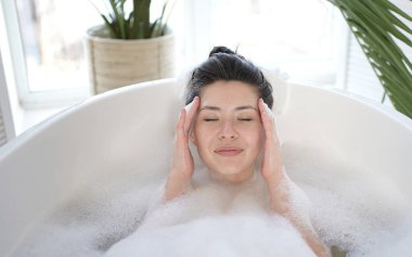 Küvette dinlenen çok ırklı çekici bir kız her gün tedaviden sonra sağlıklı, yumuşak bir yüze dokunuyor. Genç melez Asyalı kadın masaj yapıyor yüz işlemleri konseptiyle tatmin oluyor..