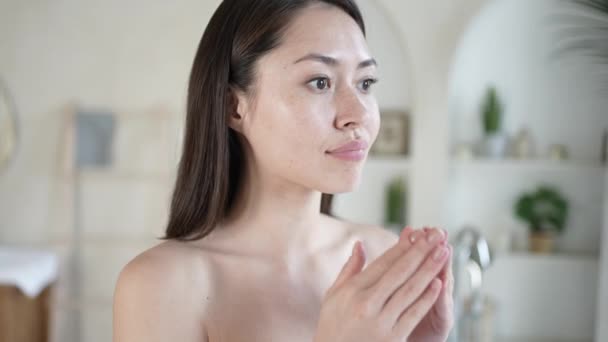Her gün tedaviden sonra aynaya bakıp sağlıklı yumuşak tene dokunan çok ırklı çekici bir kız. Genç melez Asyalı kadın masaj yapıyor yüz işlemleri konseptiyle tatmin oluyor.. — Stok video
