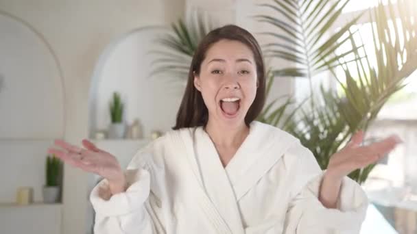 Happy young asian lady looking at camera, hearing good unbelievable news, feeling surprised and excited, showing sincere positive emotion omg reaction, during bodycare and beauty procedure in bathroom — Vídeo de stock