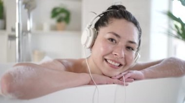 Çekici, seksi Asyalı, kulaklıklı esmer kadın sıcak bir banyonun keyfini çıkarıyor. Çok ırklı milenyum kızı rahat müzik dinliyor banyoda dinleniyor, tedavi görüyor, sağlıklı yaşam tarzı kavramları var.
