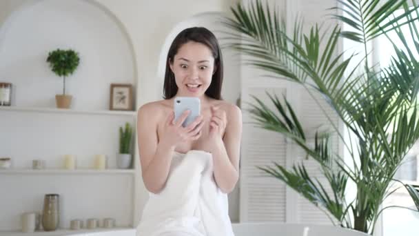 Podekscytowana wielokulturowa azjatycka dziewczyna świętująca sukces patrząc na smartfon świętujący zwycięstwo licytacji lub uzyskanie oferty e-commerce zakupy, podczas pielęgnacji ciała i zabiegu piękności w łazience — Wideo stockowe