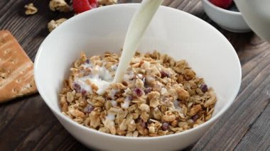 Beyaz kâseye süt dökerek sağlıklı tahıl gevreği kahvaltısı, kırsal ahşap arka planda. Müsli gevrekleri, temiz yiyecekler, vejetaryen diyeti, alerji dostu yemekler, sabah enerjisi, kilo verme konsepti.