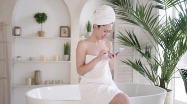 Sosyal medyada akıllı telefon sörfü yapan, haberleri kontrol eden, internet alışverişi yapan, küvette oturan çekici Asyalı kadın. Kadın, sabah saatlerinde banyoda cep telefonuyla vakit geçiriyor..