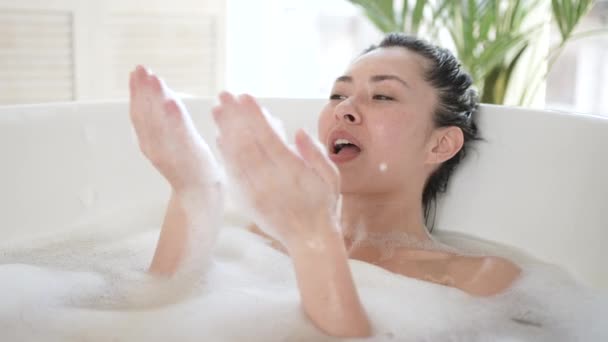 Счастливая юная азиатка играет с пеной в ванной. Счастливая миллениалка, многоэтническая женщина, получающая удовольствие от ежедневного ухода за телом в ванной комнате, косметической терапии и концепции здорового образа жизни — стоковое видео