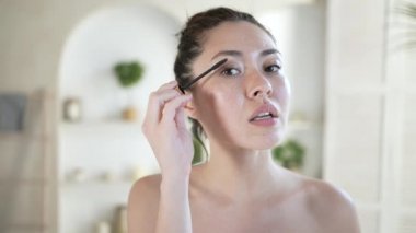 Evde banyo aynasına bakan çok ırklı çekici genç bir kadın siyah kalınlaşan rimel ile kirpiklerini boyuyor, sabahları makyaj yapan oldukça modern melez bir Asyalı kadın..