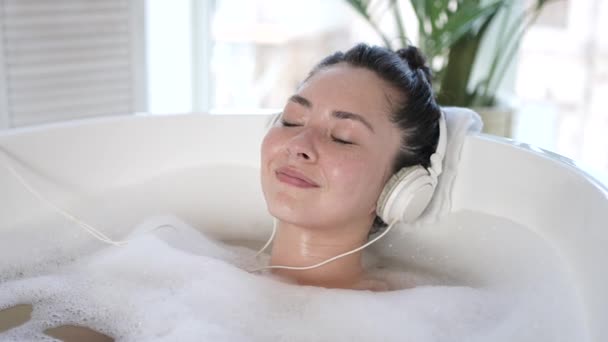 Ελκυστική νεαρή Ασιάτισσα κυρία με ακουστικά που τραγουδάει στην μπανιέρα με κλειστά μάτια. Πολυεθνική χιλιετή γυναικεία ακρόαση chill μουσική χαλάρωση στο μπάνιο, θεραπεία σώματος, έννοια του υγιεινού τρόπου ζωής — Αρχείο Βίντεο