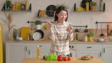 Şaşırtıcı mutlu Asyalı kız evde akıllı telefondan ecommerce alışveriş teklifi almasını kutluyor. Heyecanlı karışık yarış müşterisi cep telefonuna bakarak mobil zafer kavramını kutlayan bir uygulama kullanıyor.