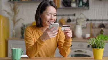 Karışık ırk kadın müşterisinin elinde banka kartı ve mobil uygulama doğrulama sürecinde kullanılan akıllı telefon var. Asyalı mutlu genç kadın internet üzerinden ödeme yapıyor ya da internet mağazasından alışveriş yapıyor.