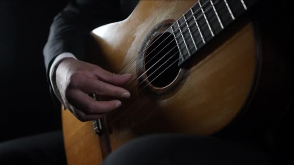 Erkek gitarist klasik akustik gitar çalar, akorları öğrenir, kendi kendini eğiten bir telli çalgı çalar. Profesyonel müzisyen siyah arkaplan üzerinde mükemmel bir teknik sergiliyor. — Stok video