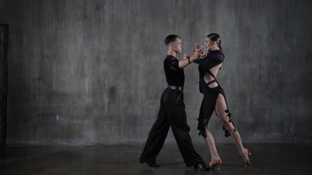 Siyah elbiseli genç dans salonu çifti stüdyo arka planında şehvetli bir şekilde dans ediyor. Latin dansı yapan profesyonel dansçılar. Balo dansı konsepti. İnsani duygular - aşk ve tutku — Stok video