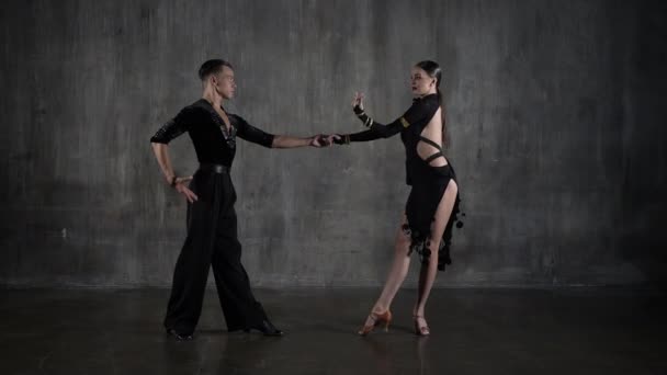 O jovem casal de salão de baile de dança milenar em vestido preto dançando em pose sensual no fundo do estúdio. Dançarinos profissionais dançando latino. Conceito de dança Hobby. Emoções humanas - amor e paixão — Vídeo de Stock