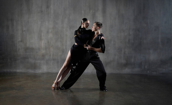 Молодая танцевальная бальная пара тысячелетия в черном платье танцует в чувственной позе на студийном фоне. Профессиональные танцоры танцуют латино. Концепция танцев. Человеческие эмоции - любовь и страсть