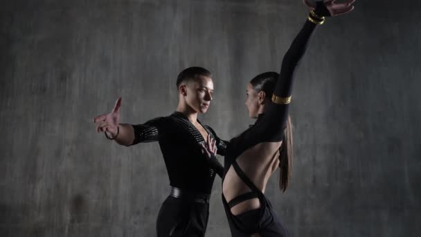 La joven pareja milenaria de baile de salón en vestido negro bailando en pose sensual sobre fondo de estudio. Bailarines profesionales bailando latino. Concepto de baile hobby. Emociones humanas - amor y pasión — Vídeo de stock
