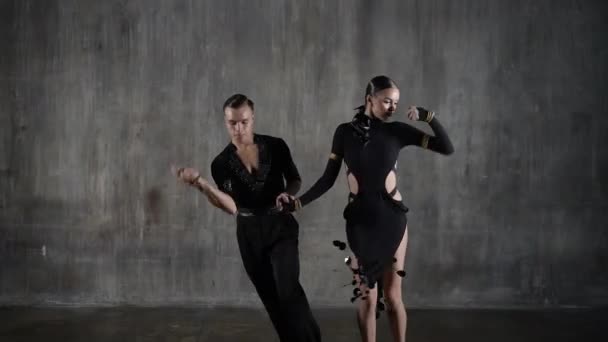 O jovem casal de baile de dança milenar ativo em vestido preto dançando em pose sensual sobre o fundo do estúdio. Dançarinos profissionais dançando latino. Conceito de dança Hobby. Emoções humanas, paixão amorosa — Vídeo de Stock