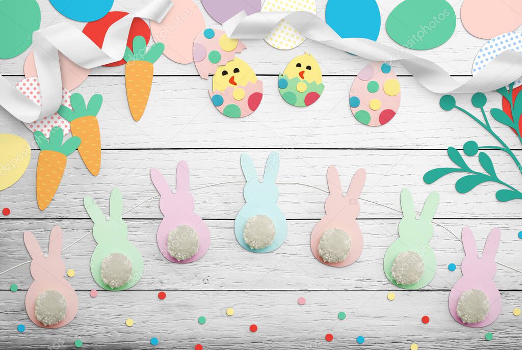 Easter handmade crafts of multi-colored paper, cardboard, eggs, ribbons, carrots, bunnies with pom poms. Child art creativity on wooden table. Inscription Happy Easter. Top view, close up, copy space