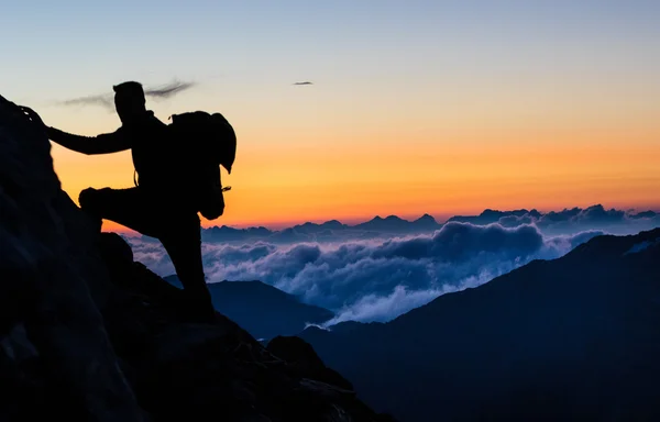 นักปีนเขาไปถึงยอดภูเขาเพื่อพระอาทิตย์ขึ้นเหนือเมฆ — ภาพถ่ายสต็อก