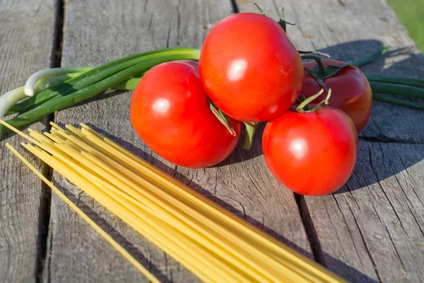 La pasta y los tomates sobre la rama a la mesa vieja de madera . —  Fotos de Stock