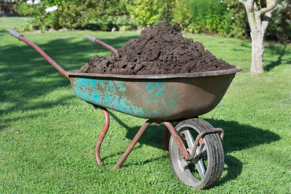 Brouette pleine de compost sur pelouse verte dans le jardin . — Photo