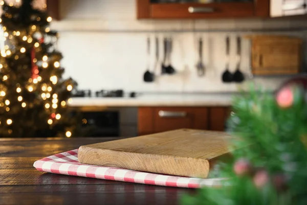 Wooden tabletop with cutting board and blurred kitchen decorated Christmas tree for holiday. Space for display your products.