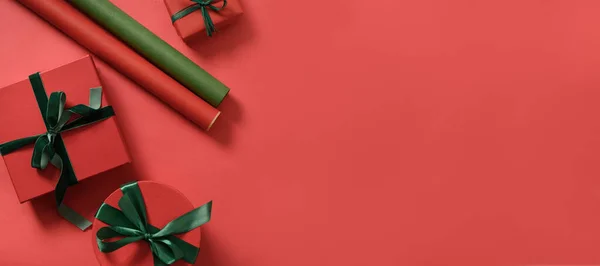Christmas banner with red and green gifts, paper rolls on red. Preparation and wrapping presents for holidays. Top view with copy space.