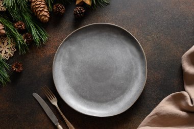 Boş gri tabağı ve kahverengi masasında ahşap dekoru olan Noel masası. Kırsal ev tarzı. Üst manzara, düz uzanma.