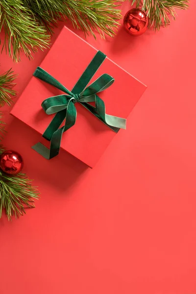 装飾的な緑のベルベットリボン 赤い表面に常緑の枝を持つクリスマスの赤いギフト 最上階だ 垂直クリスマスグリーティングカード — ストック写真