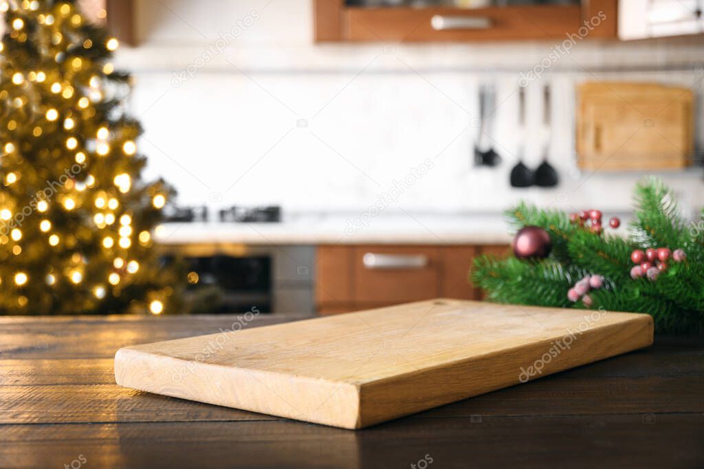 Empty cutting board on wooden tabletop with and blurred holiday kitchen decorated Christmas tree. Space for your products.