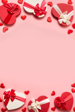 Sevgililer Günü 'nde pembe arka planda kırmızı kalpler olan romantik hediyeler. Düz yatıyordu. Kopyalama alanı olan dikey tebrik kartı.