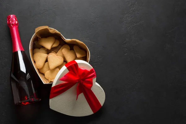 Bottle of sparkling wine, cookies and gift as heart on black background. Valentine\'s Day Greeting card. View from above. Space for text.