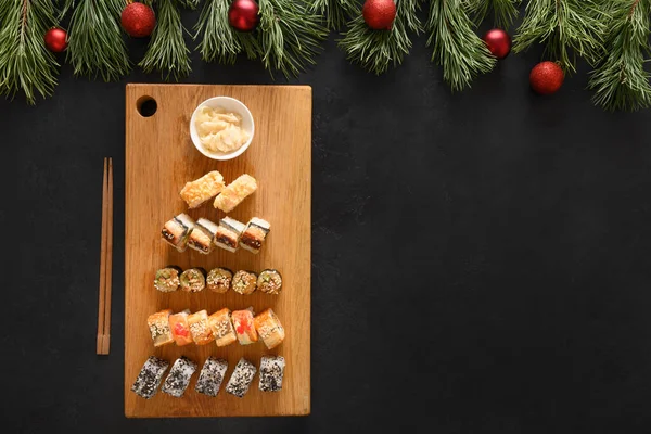 Sushi satt i tallerken som juletre pyntet med grangreiner på svart. – stockfoto