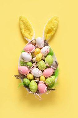 Renkli paskalya yumurtaları tabakta ve tavşan kulakları sarıda. Paskalya tebrik kartı.