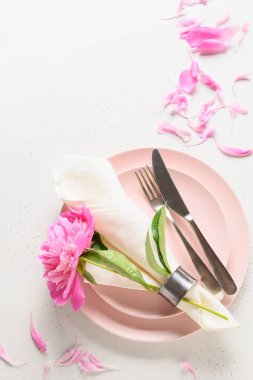 Beyaz masa üzerinde pembe şakayık çiçekleri olan şenlikli yaz sofrası. Dikey format. Yukarıdan görüntüle.