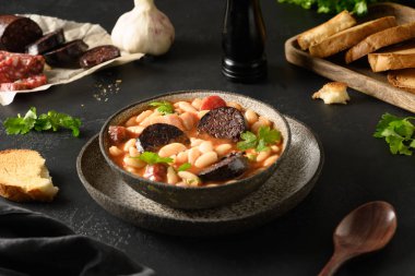 Sucuklu, morilyalı, sosisli, haricot sosisli, siyah arka planda taze tost servisi yapan popüler İspanyol efsanesi. Asturian fasulye güveci. Kapat..