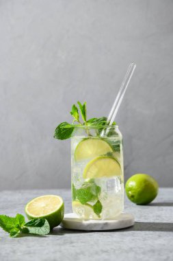 Beyaz rom, soda, esmer şeker, kireç ve gri arkaplanda naneli mojito kokteyli. Dikey. Kapat..
