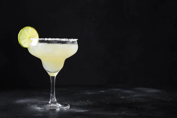 Classic Margarita cocktail with lime juice and ice cube on black background.