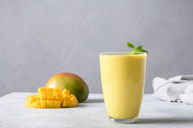 Sağlıklı organik mango lassi, donmuş buzlu içecek ya da gri arka planda meyve suyu. Hint sağIıklı ve mangolu soğuk bir içecek. Yoğurttan, sudan, baharatlardan, meyvelerden ve buzdan yapılmış taze Lassi. Yoğurtlu ve taze hintli vegan içeceği. 