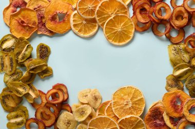 Kurutulmuş erik, kivi, şeftali, mavi arka planda portakallı meyve cipsi ve mesaj. Atıştırmalık vejetaryen şekersiz yiyecek. Yukarıdan görüntüle.