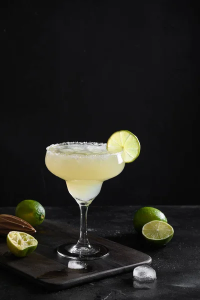 Classic Margarita cocktail with lime juice and ice cube on black background. Vertical orientation.
