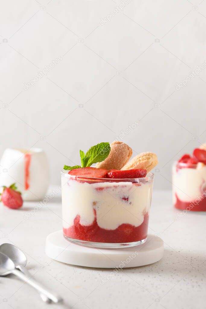 Layered dessert in glass jars with cookie savoyardi, mascarpone and whipped cream decorated strawberries