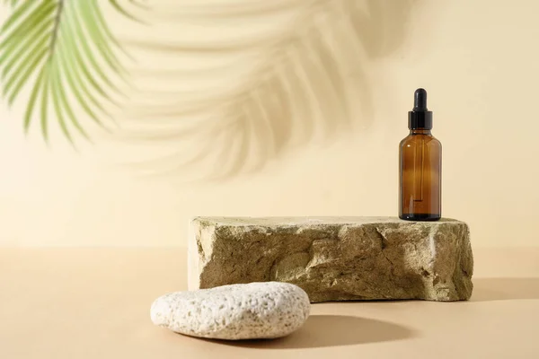 Minimum modern SPA kompozisyonu, cam şişedeki kozmetik yağla taşın üzerine koyulmuş ve gölgesi tarafsız bej arka planda..