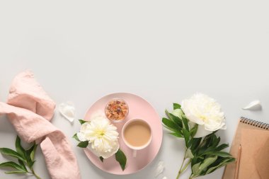 Kahve fincanı, eskiz defteri ve gri ofis masasında beyaz şakayık çiçekleri olan romantik yaz kahvaltısı. Üst manzara, düz uzanma.