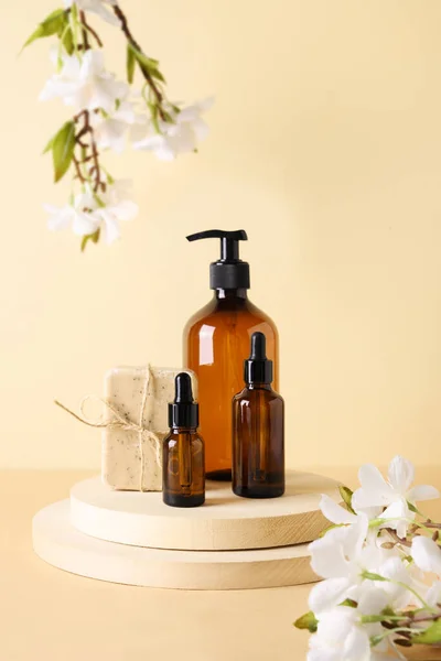 Cosmetics dark amber bottles with natural soap and spring flowers on wooden podium.