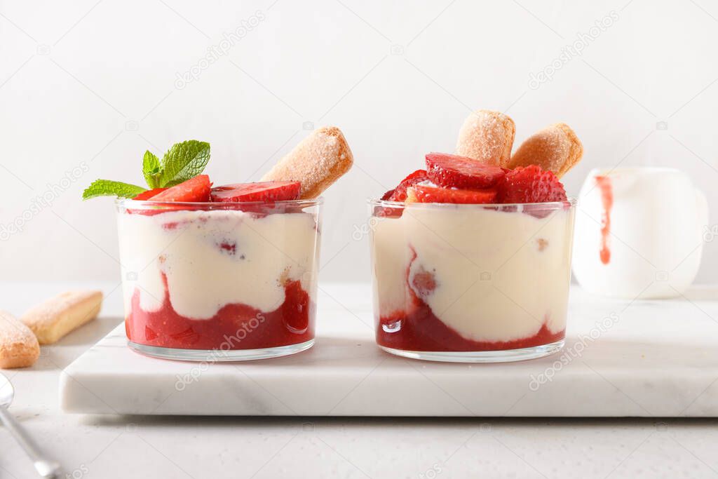 Layered dessert in glass jars with cookie savoyardi, mascarpone and whipped cream decorated strawberries