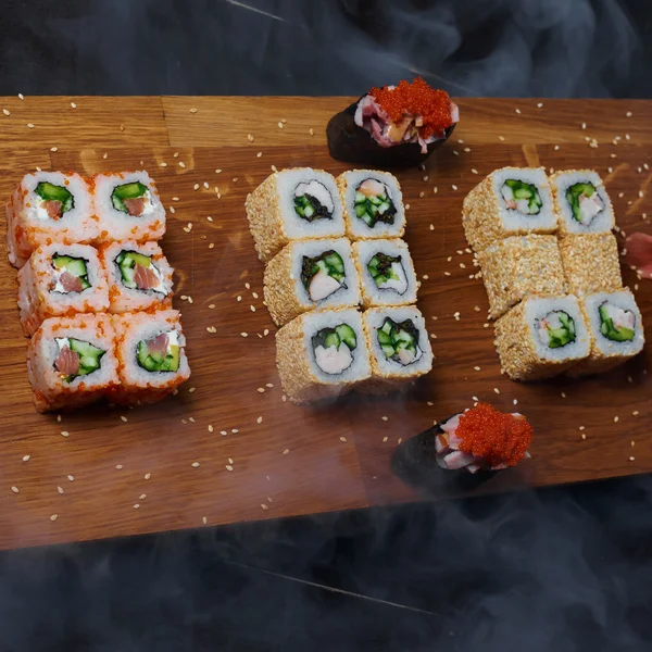 Duman ile koyu arka plan üzerinde ahşap bir gemide kümesi suşi rulo