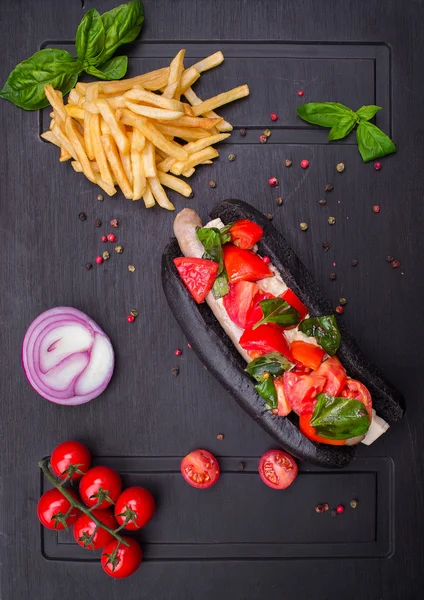 Sosisli sandviç gelen siyah ekmek domates fesleğen ve karanlık bir tahta üzerinde patates kızartması ile